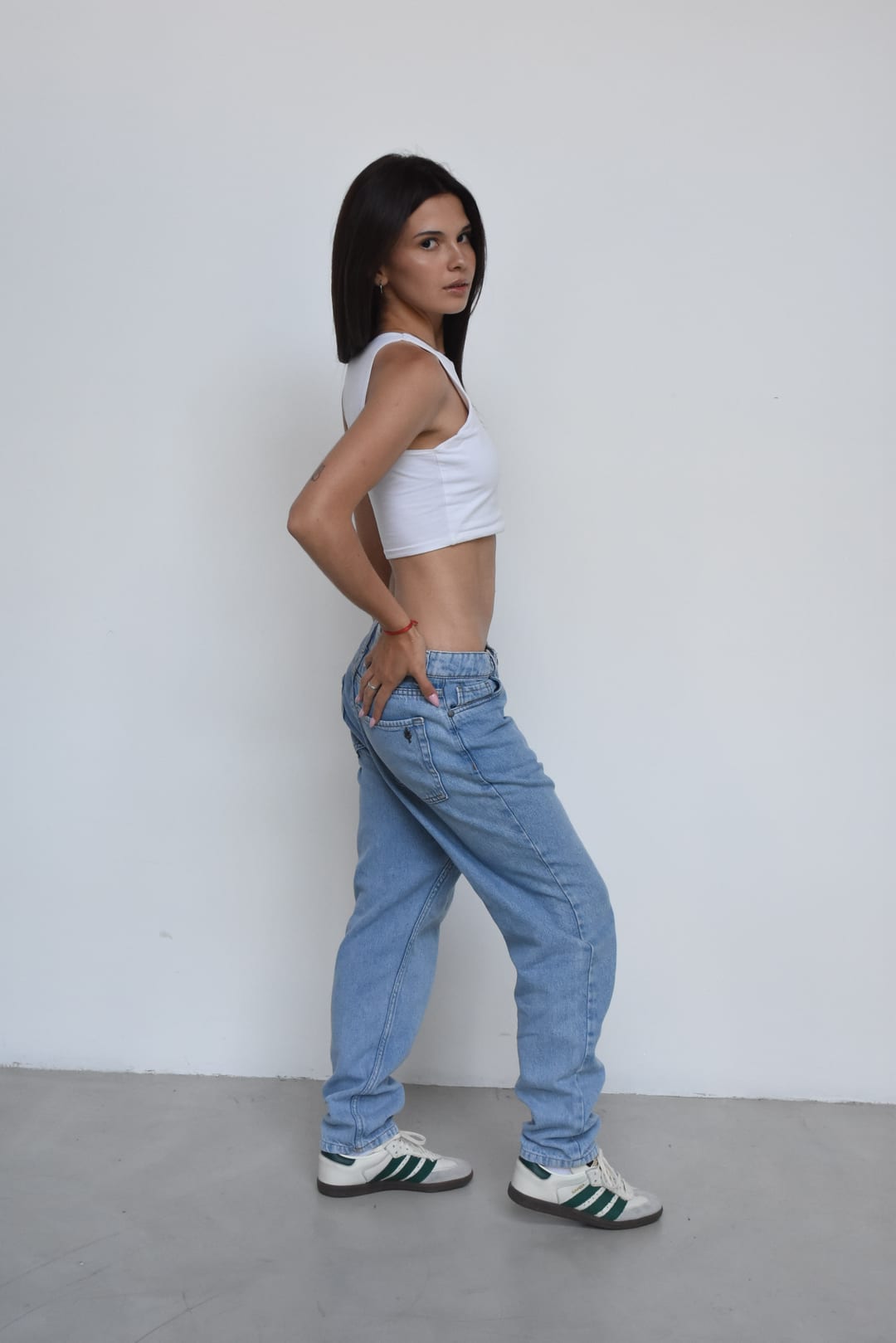 Foto de cuerpo entero de Tatiana Gramajo con top blanco, jean celeste y zapatillas, mirando por sobre el hombro