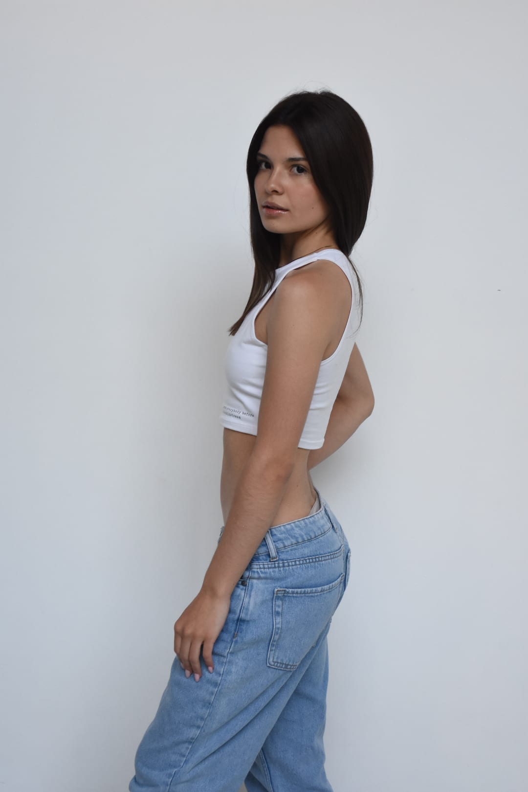Foto de tres cuartos de Tatiana Gramajo con musculosa blanca y jean, mirando a cámara por sobre el hombro